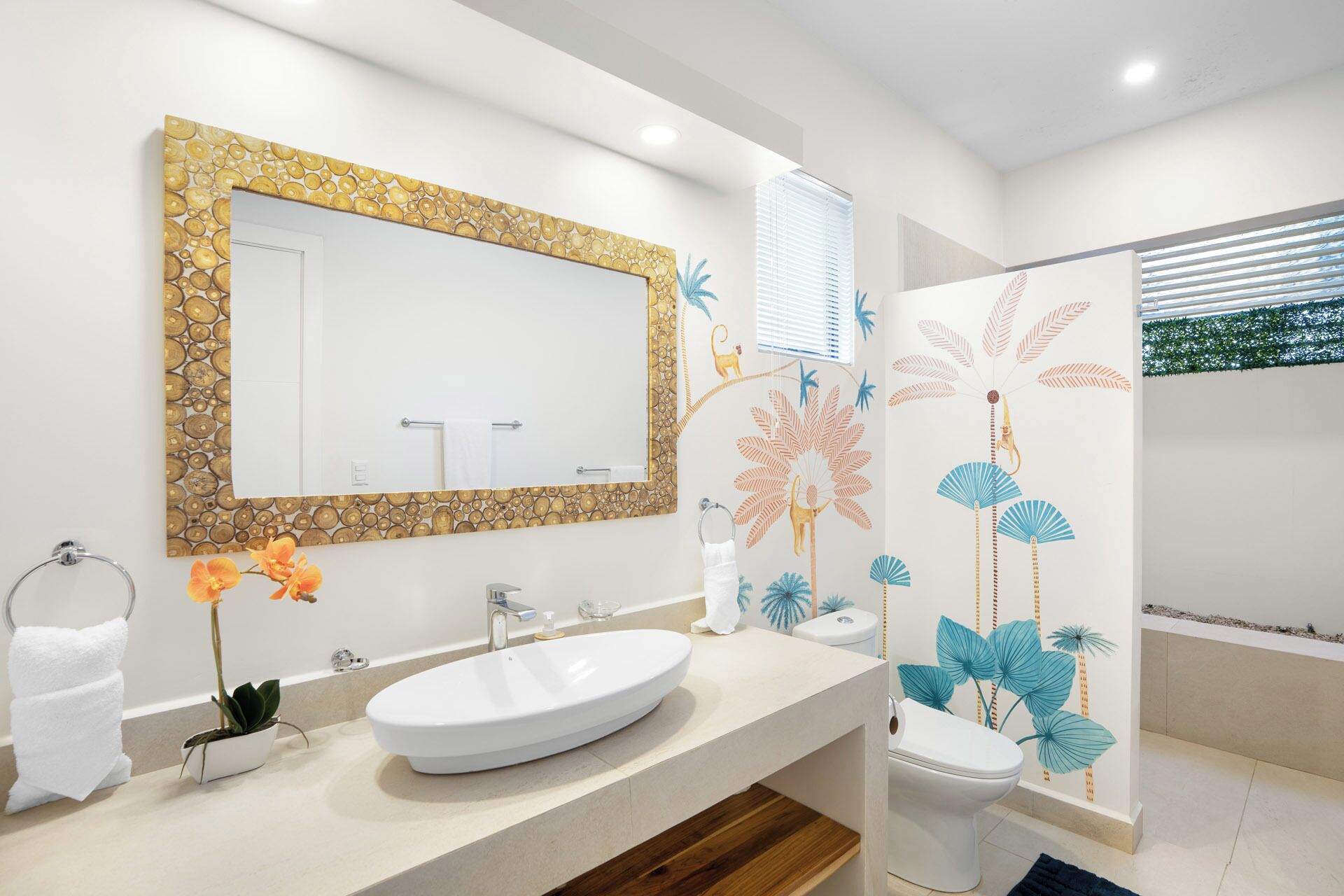 Un baño moderno con un espejo grande, un lavamanos blanco, un inodoro y una ducha con detalles decorativos en la pared.