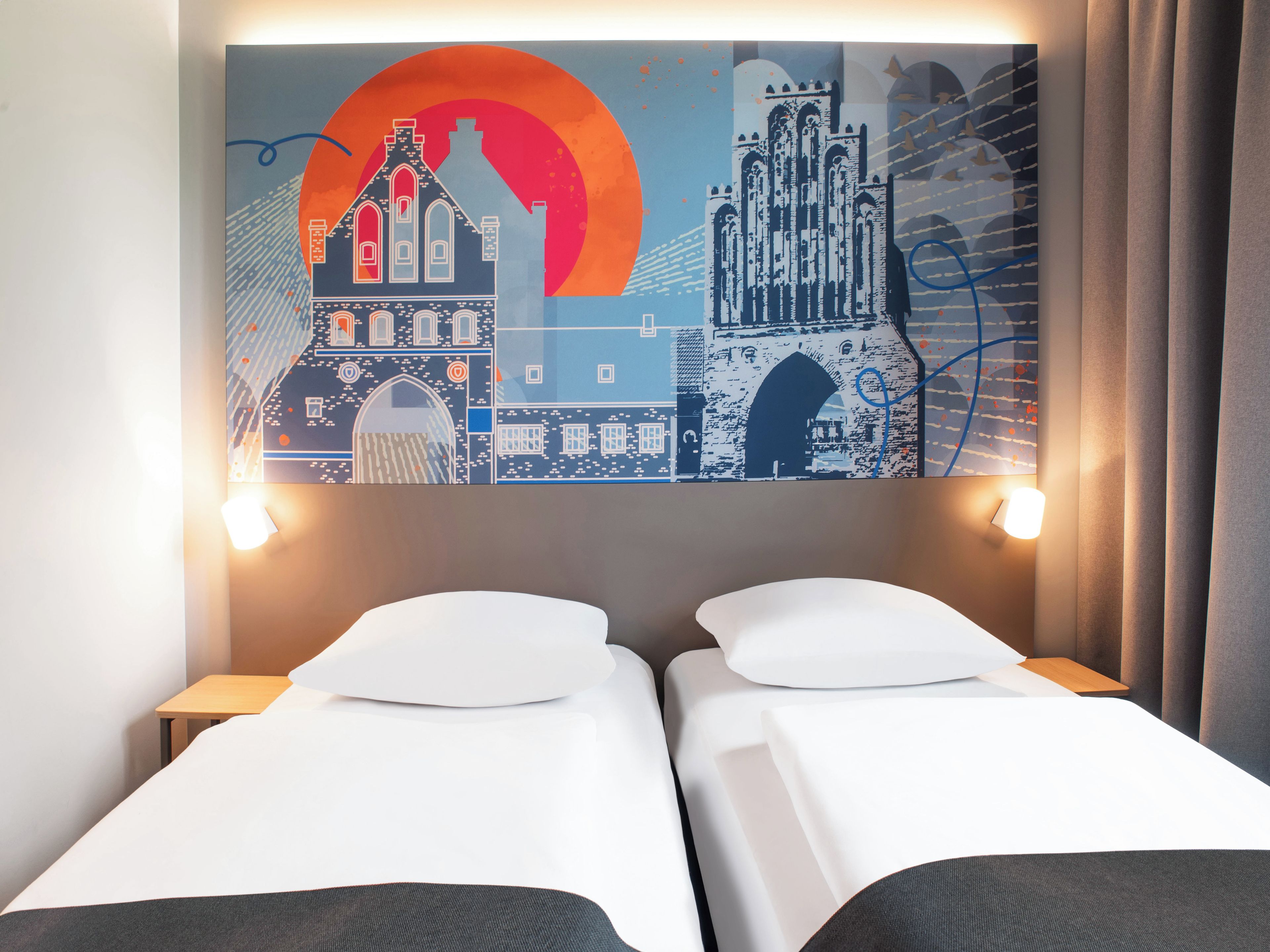 Une chambre d’hôtel avec deux lits, une grande fresque murale et une table de chevet avec une lampe.