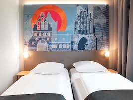 Habitación de hotel con dos camas, un mural grande en la pared y una mesita de noche con una lámpara.