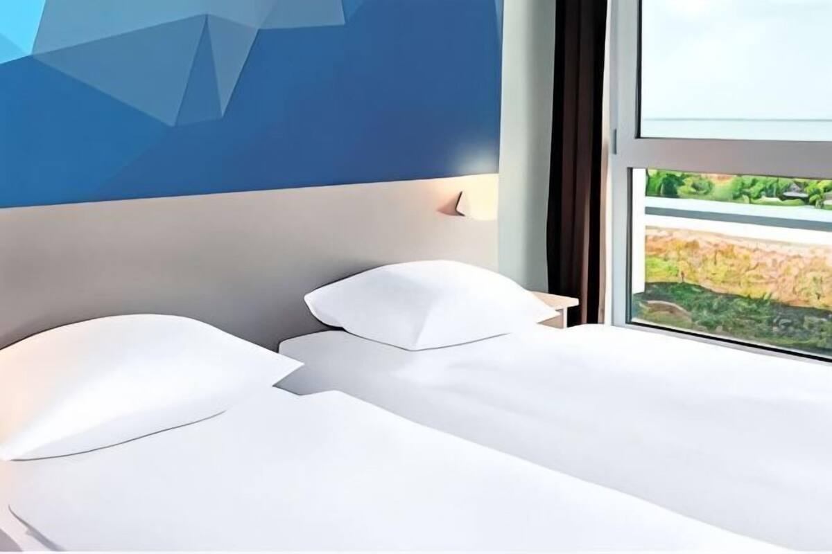 A modern hotel room with a bed, a nightstand, and a window with a view of greenery.
