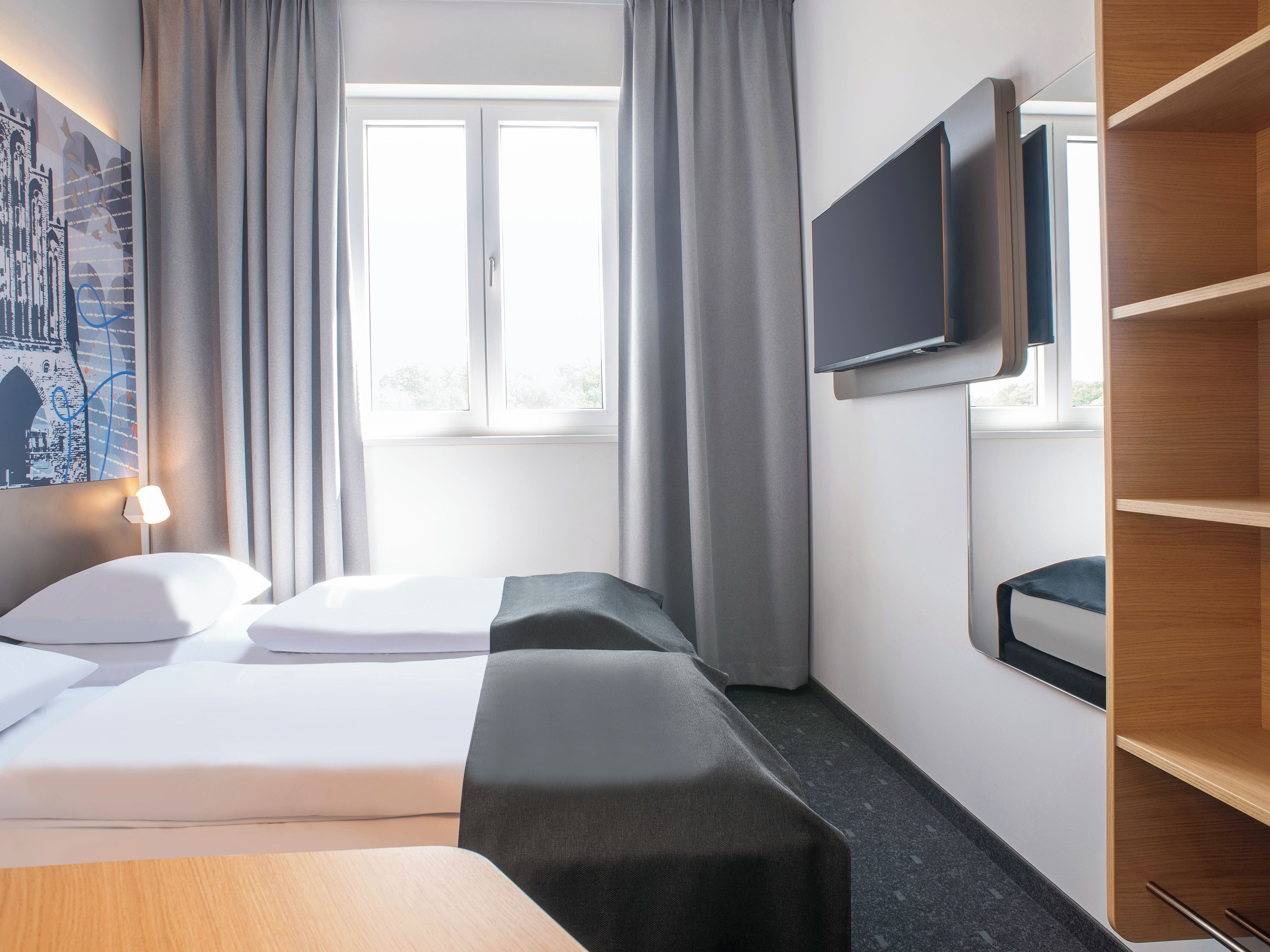 A hotel room with a bed, a TV mounted on the wall, and a window with curtains.