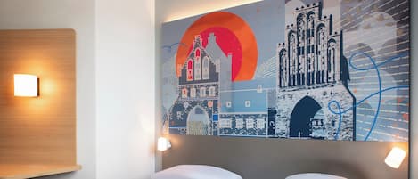 Ein Hotelzimmer mit einem Bett, zwei Nachttischlampen und einer Wand mit Stadtbildkunstwerk.