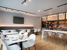 Un comedor moderno con mesas, sillas, un mostrador de buffet y un televisor de pantalla plana montado en la pared.