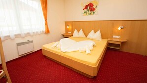Habitación de hotel con una cama, dos mesitas de noche, un calentador de pared, una ventana con cortinas y un cuadro.