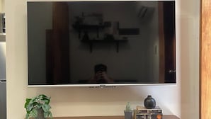 A flat-screen TV mounted on a wall above a wooden shelf with decorative items. - 01 Easy Access Stay, Minutes from Airport on Main Road (Lapu-Lapu City)