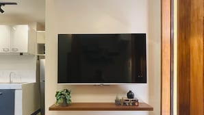 A modern kitchen with a built-in TV, a wooden shelf with decorative items, and a view of the adjacent living area. - 01 Easy Access Stay, Minutes from Airport on Main Road (Lapu-Lapu City)