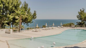A swimming pool with lounge chairs and umbrellas, surrounded by trees and overlooking the sea. - Hotiday Room Collection - Mattinata Faraglioni (Mattinata)