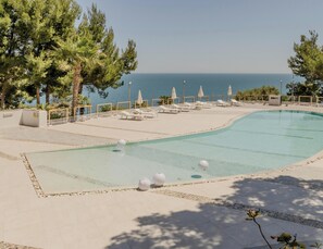 A swimming pool with lounge chairs and umbrellas, surrounded by trees and a view of the sea. - Hotiday Room Collection - Mattinata Faraglioni (Mattinata)