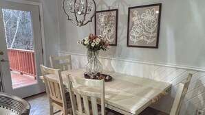 A dining area with a wooden table and chairs, a vase with flowers, and framed artwork on the wall.