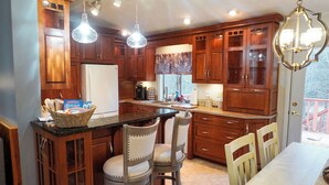 A kitchen with wooden cabinets, a central island with chairs, pendant lights, and a view of the outdoors.