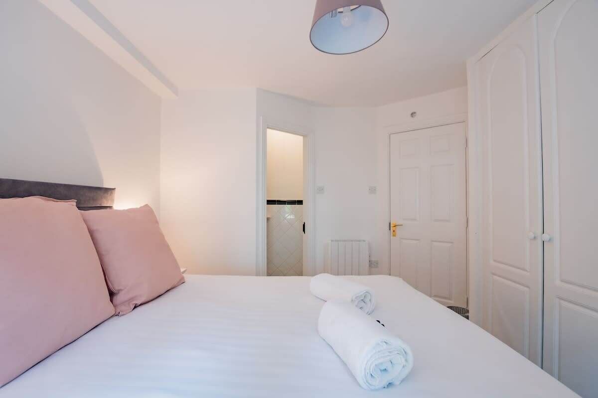 A hotel room with a bed, a rolled towel, and a door.