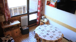 A cozy room with a round table covered with a heart-patterned tablecloth, a wooden cabinet, a small shelf with items, and a TV mounted on the wall. - Hameau des 4 Saisons Hsg226 Mountain & View 6 Pers (Chatel)