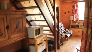 A rustic wooden interior with a wooden staircase, a sofa with a cow print cover, a wooden cabinet with a decorative panel, and a small table with a lamp. - Hameau des 4 Saisons Hsg226 Mountain & View 6 Pers (Chatel)