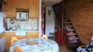 A kitchen with wooden cabinets, a microwave, and a sink. There is a dining table with a tablecloth and chairs. A staircase leads to another room. - Hameau des 4 Saisons Hsg226 Mountain & View 6 Pers (Chatel)