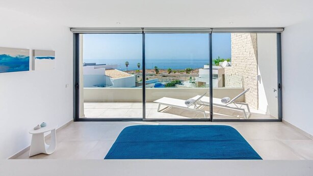 A bedroom with a large sliding glass door leading to a balcony with a pool and lounge chairs. - 4-bedroom modern villa with private pool and spectacular views! (La Caleta)