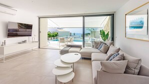 A modern living room with a sofa, a TV, and a dining area with a view of the sea. - 4-bedroom modern villa with private pool and spectacular views! (La Caleta)