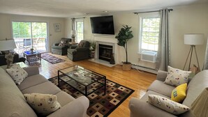 A living room with a fireplace, sofas, a coffee table, and a TV. - Summer Beach Rental w/ Beach Pass - 3 bed/3 bath (Charlestown)