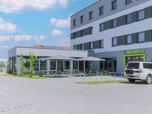 Ein modernes Hotel mit Glasfassade, Außenbereich zum Sitzen und einem weißen Lieferwagen davor.