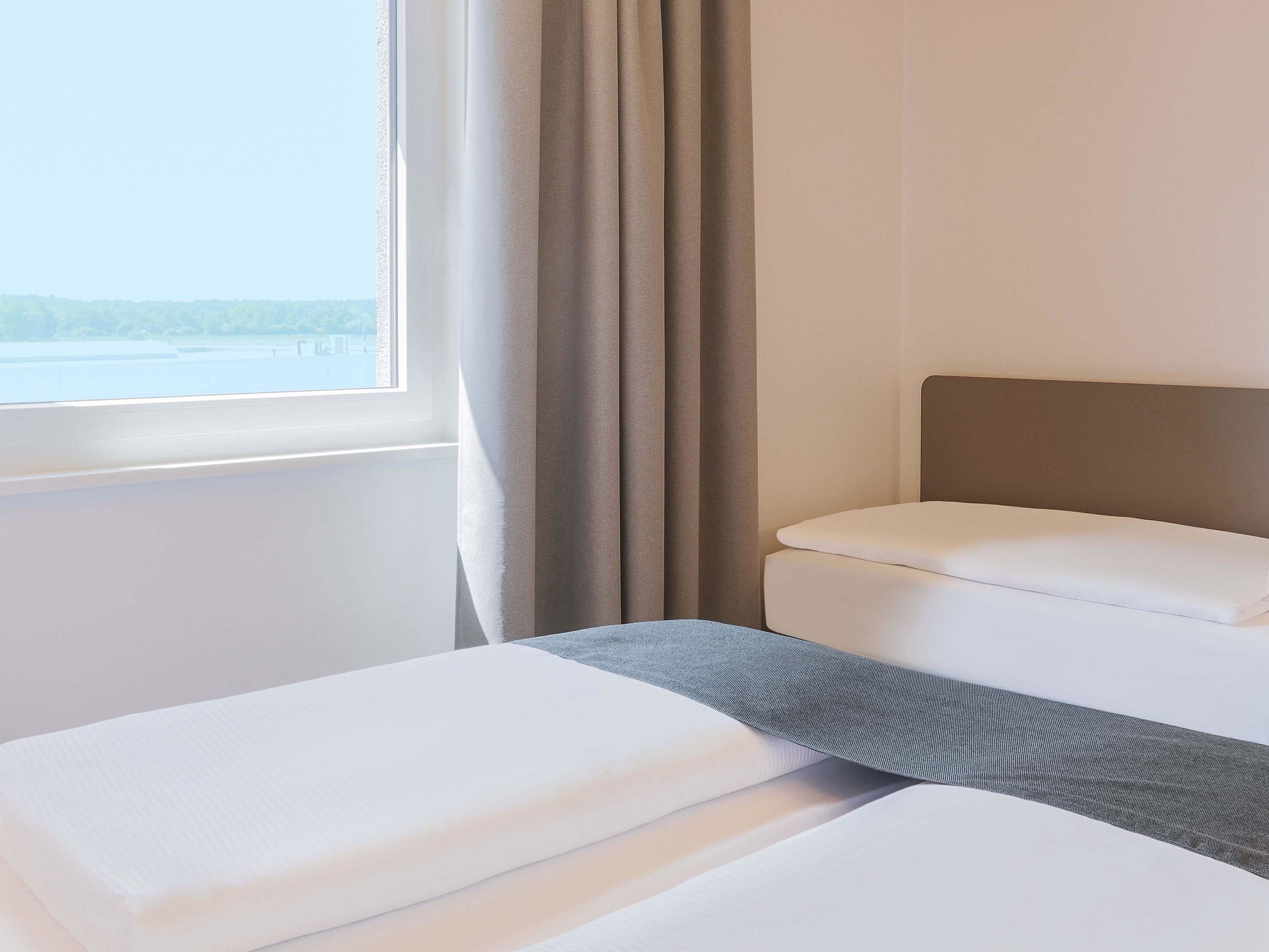 Una habitació d'hotel amb un llit, una finestra amb cortines i vistes a l'exterior.