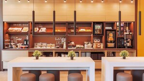 Un café moderne avec un comptoir en bois où sont exposées des pâtisseries et du matériel pour préparer le café. On y trouve des tables avec des tabourets et une machine à café.