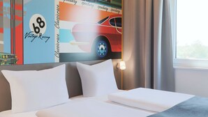 Habitación de hotel con cama, almohadas, mesita de noche, lámpara y ventana con cortinas.