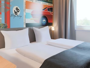 Une chambre d’hôtel avec un lit, des oreillers, une table de chevet, une lampe et une fenêtre avec des rideaux.