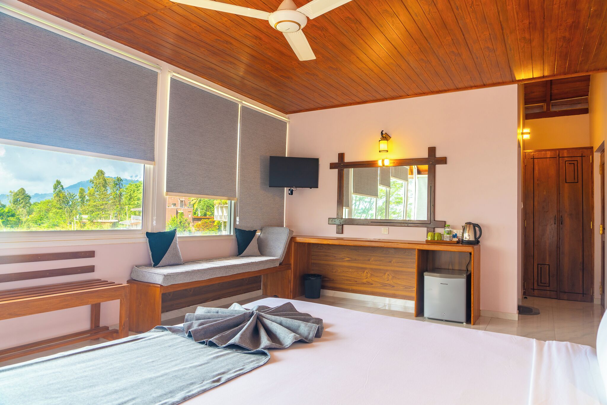 Ein Schlafzimmer mit Bett, einer Bank, einem Schreibtisch, einem Fernseher und Blick ins Freie.