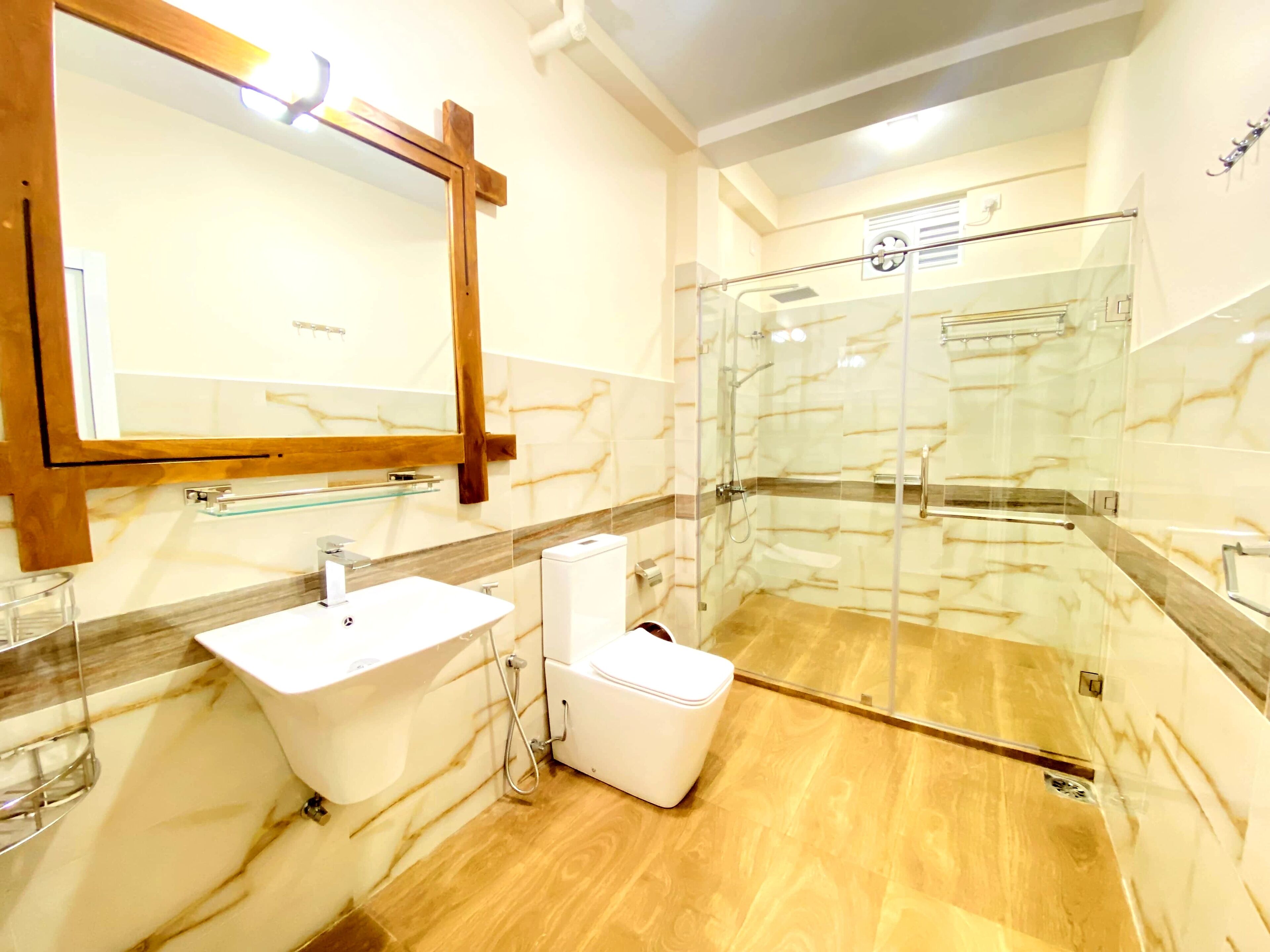 A bathroom with a marble vanity, a toilet, a glass shower enclosure, and a wooden-framed mirror.