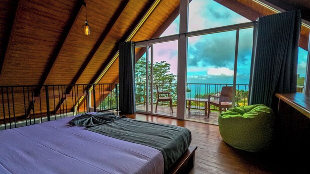 A bedroom with a large bed, a green bean bag, and a balcony with a view. - Mount Hunt Resort (Beragala)