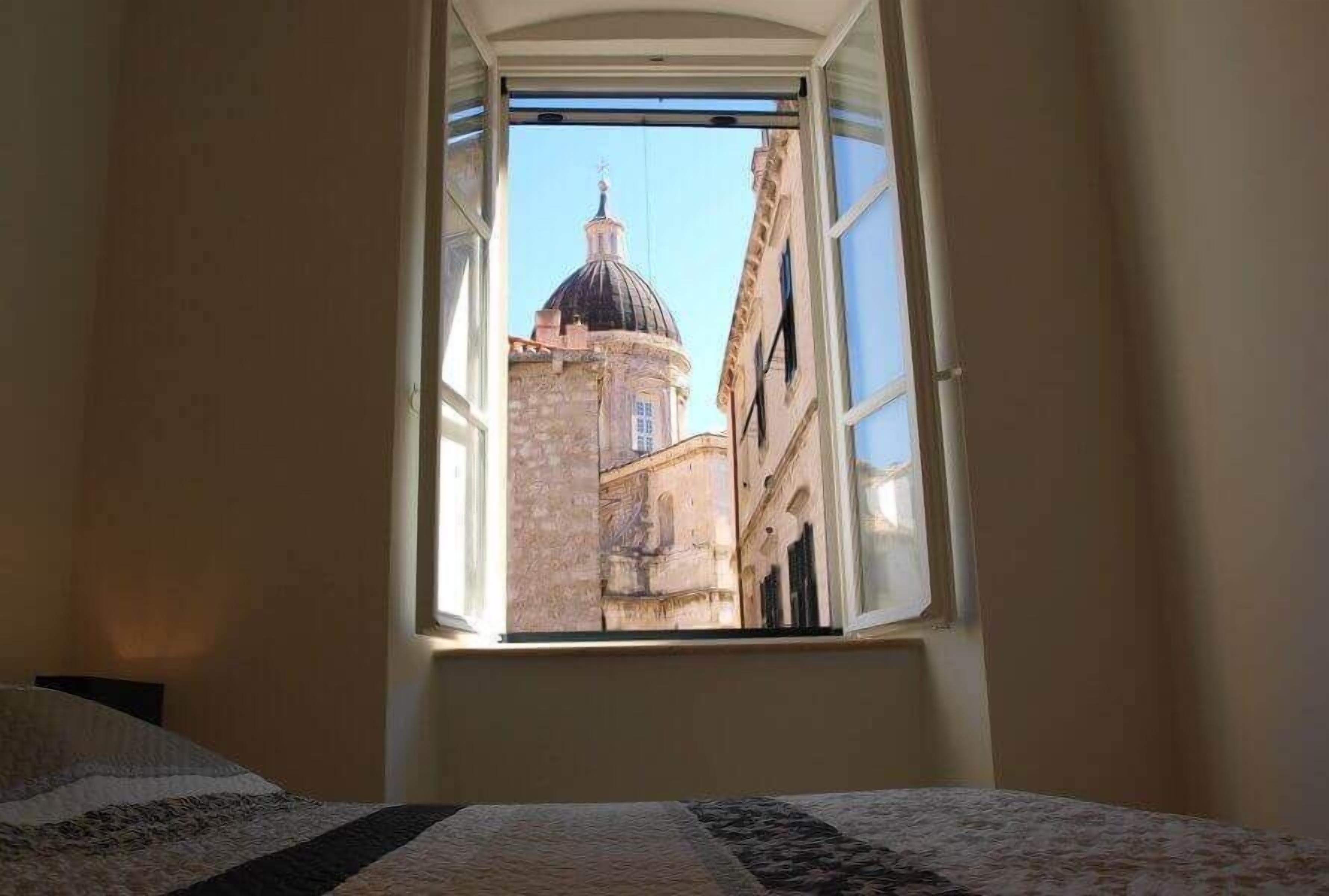 Une chambre avec un lit et une fenêtre donnant sur un bâtiment surmonté d’un dôme.
