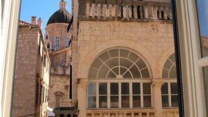 A narrow street with historic stone buildings, including a building with a large arched window and a dome structure in the background. - La Dolce Vita-Old Town (Dubrovnik)