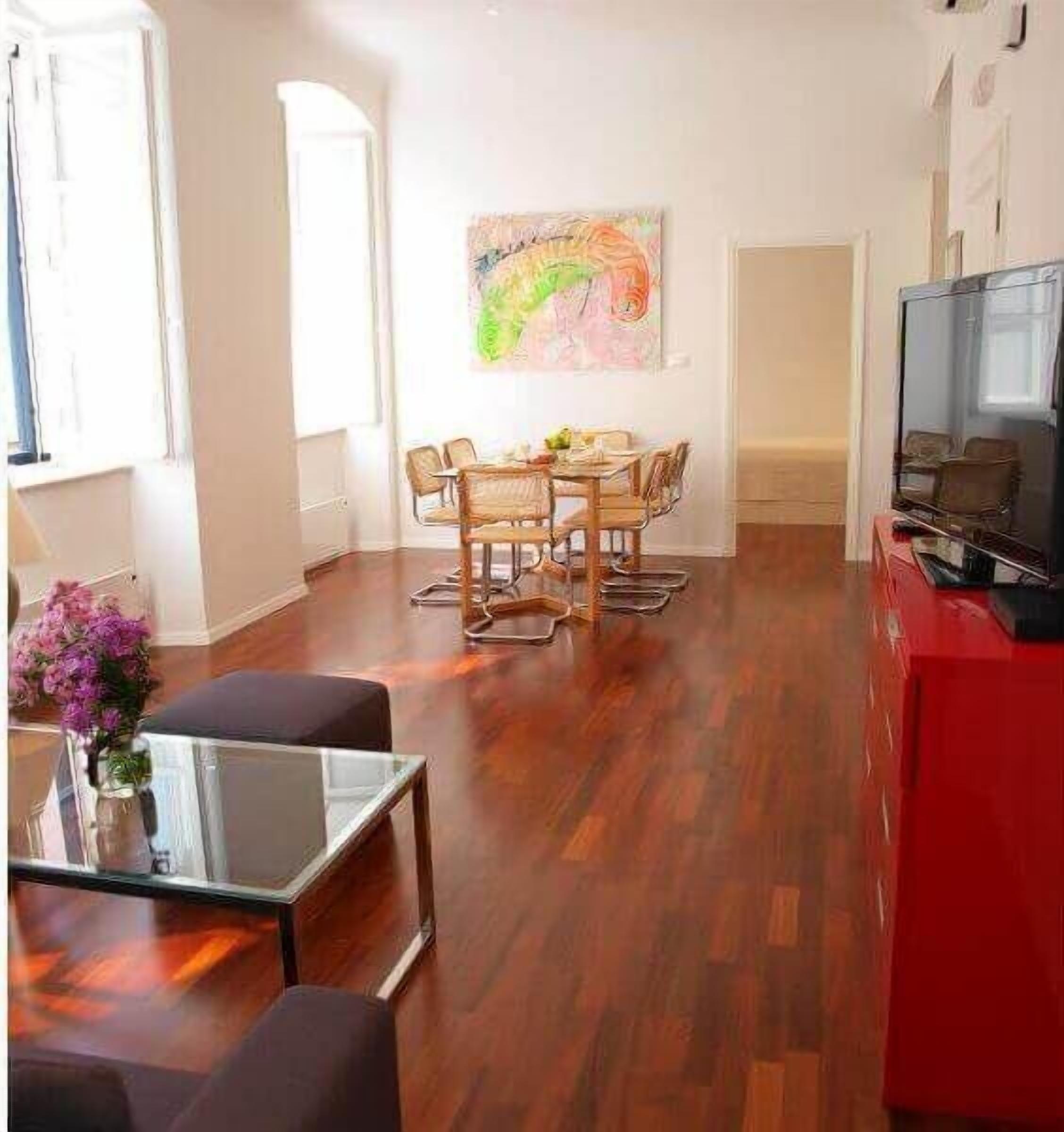 A living room with a dining table, chairs, a TV, and a painting on the wall.