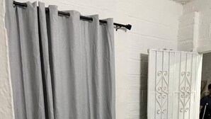 A room with a glass table and wooden chairs, a grey curtain, and a white door with decorative metalwork.