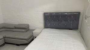A bedroom with a bed, a gray sofa, and a white brick wall.