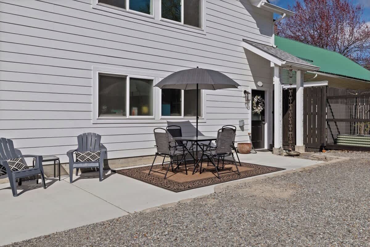 A house with a patio area featuring a table and chairs, a small rug, and a decorative umbrella.