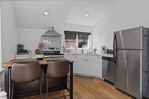 Une cuisine moderne dotée d’un réfrigérateur en acier inoxydable, d’un îlot central avec deux chaises, d’une cuisinière et d’une fenêtre donnant sur un jardin.