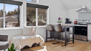 A modern kitchen with a large window, a dining area with two chairs, and a cozy seating area with a fur throw.