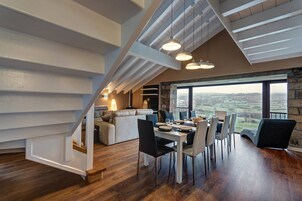 Un área de comedor con vistas al campo, una chimenea de piedra y una escalera moderna.