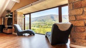 Un'ampia stanza con una grande finestra che si affaccia su un paesaggio montuoso. Sono presenti due poltrone nere con decorazioni in pelliccia bianca e un mobile porta TV in legno sotto la finestra.