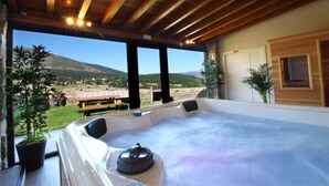 Una vasca idromassaggio con vista su un paesaggio montuoso, travi in legno a soffitto e piante in vaso.