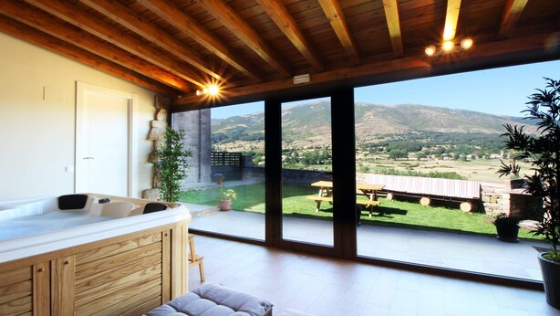 Una camera moderna con soffitto in legno, una grande porta scorrevole in vetro che dà su un patio e vista su un paesaggio montuoso.