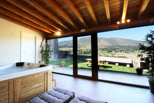 Una habitación moderna con techo de madera, un amplio ventanal corredera que da a un patio y vistas de un paisaje montañoso.