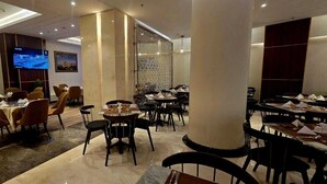 Ein Restaurant mit mehreren Essbereichen, darunter eine Bar/Lounge mit runden Tischen und Stühlen sowie ein separater Speisesaal mit rechteckigen Tischen.