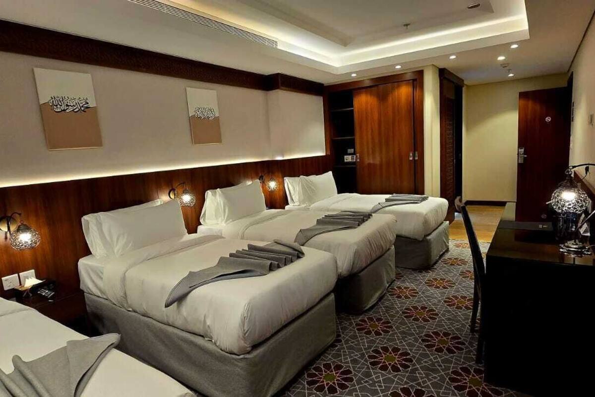 A hotel room with two beds, a TV, a minibar, and a decorative wall with calligraphy.