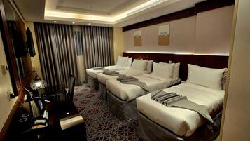 A hotel room with two beds, a desk with a lamp, a television, and a patterned carpet.
