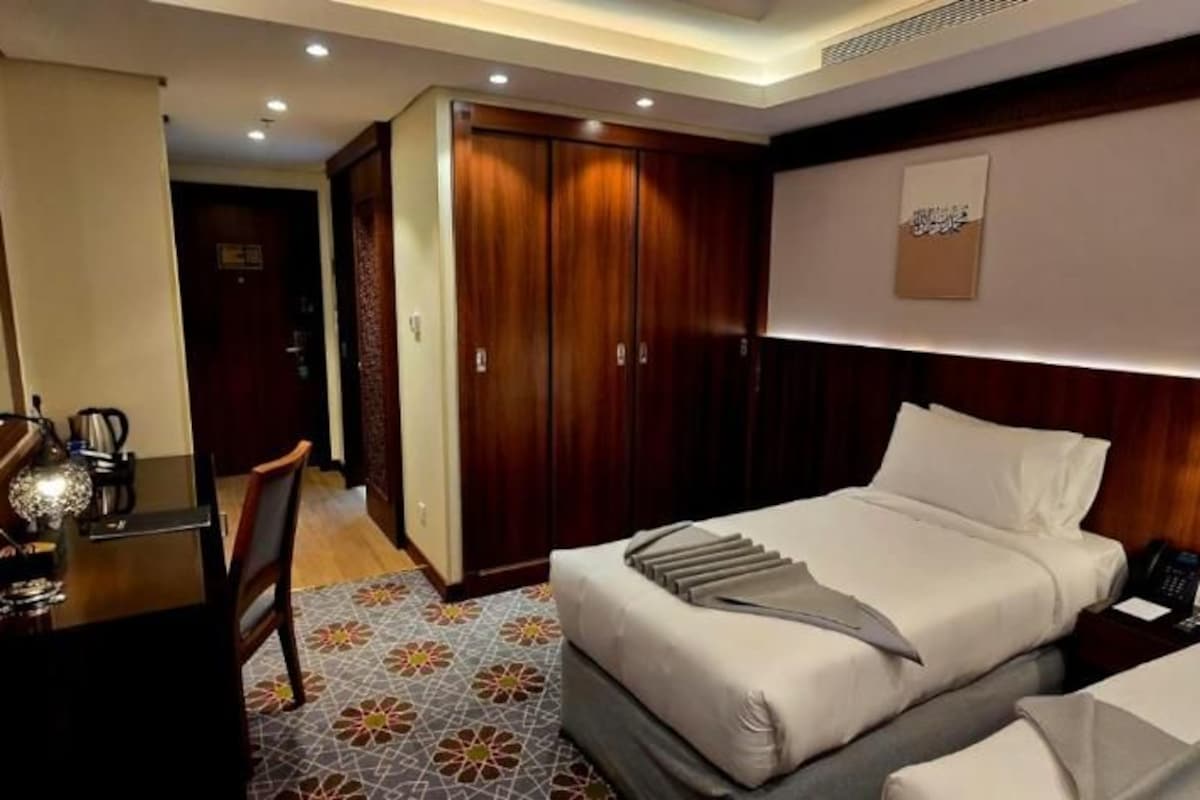 A hotel room with a TV, a desk with a chair, two beds, and a wardrobe.