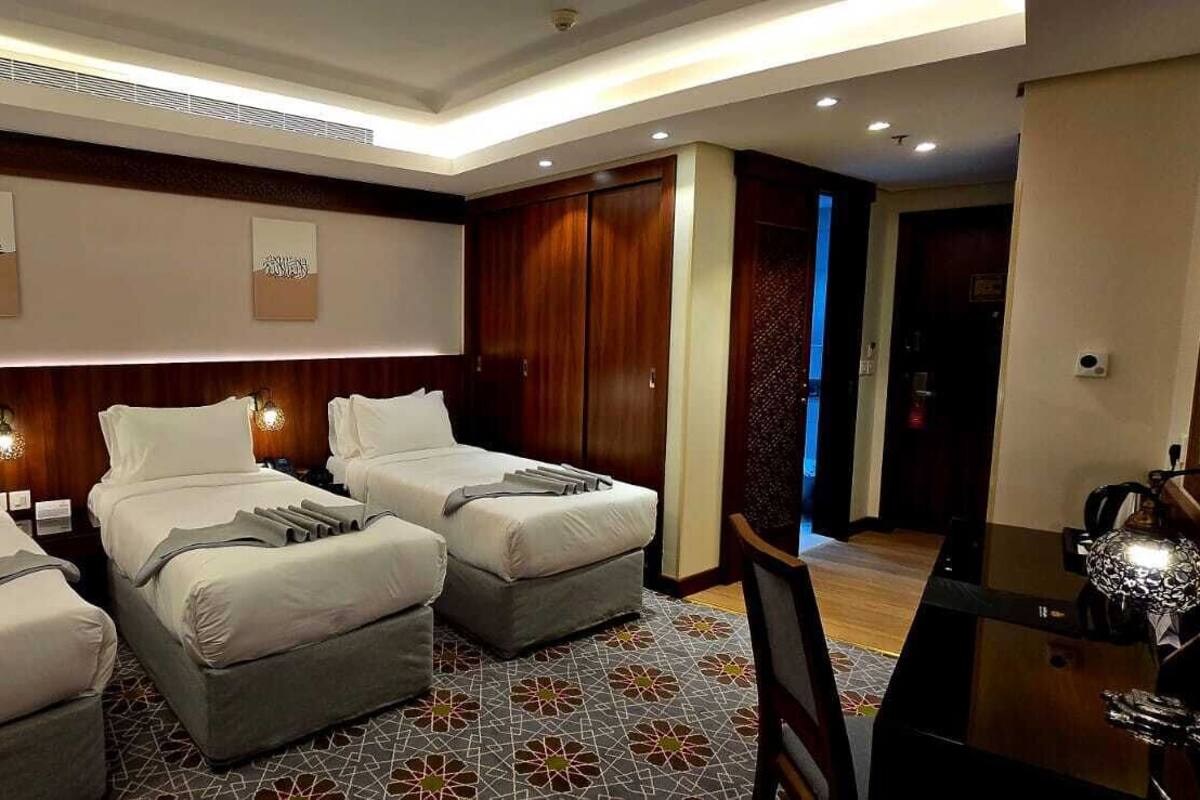 A hotel room with two single beds, a desk with a lamp, and a wardrobe.