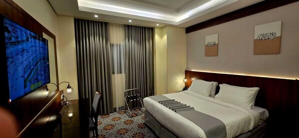 A hotel room with a large bed, a TV, a desk with a chair, and a staircase.