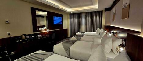 A hotel room with a large bed, a desk with a computer, a TV, and a minibar.