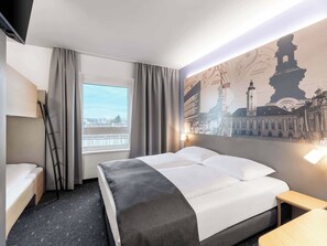 A hotel room with a bed, a desk, a chair, a window with curtains, and a wall with a cityscape mural. - B&B HOTEL St. Pölten (St. Pölten)